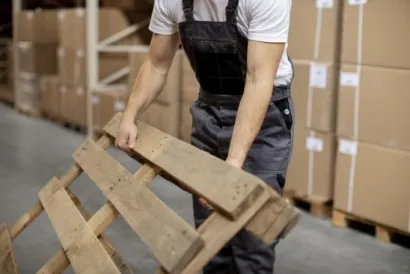 Operador carrega um palete com caixas de papelão arqueadas ao fundo. Operador carrega um palete com caixas de papelão arqueadas ao fundo.